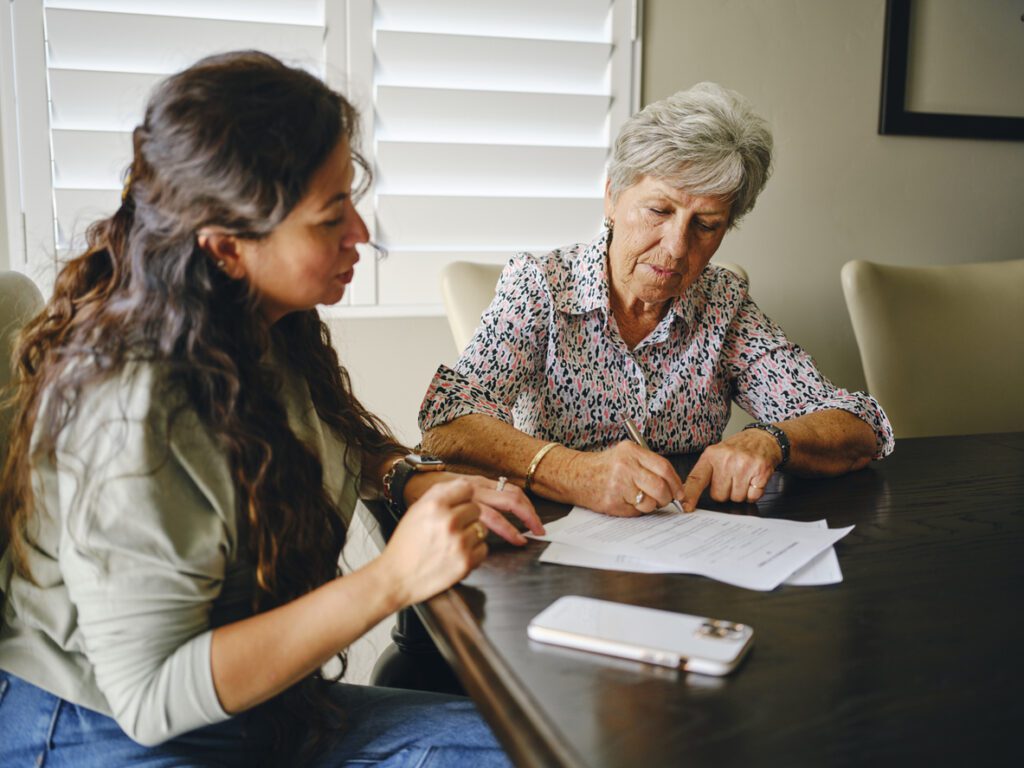 A Hispanic woman, helping a senior aged woman prepare financial documents - a representation of choosing a power of attorney